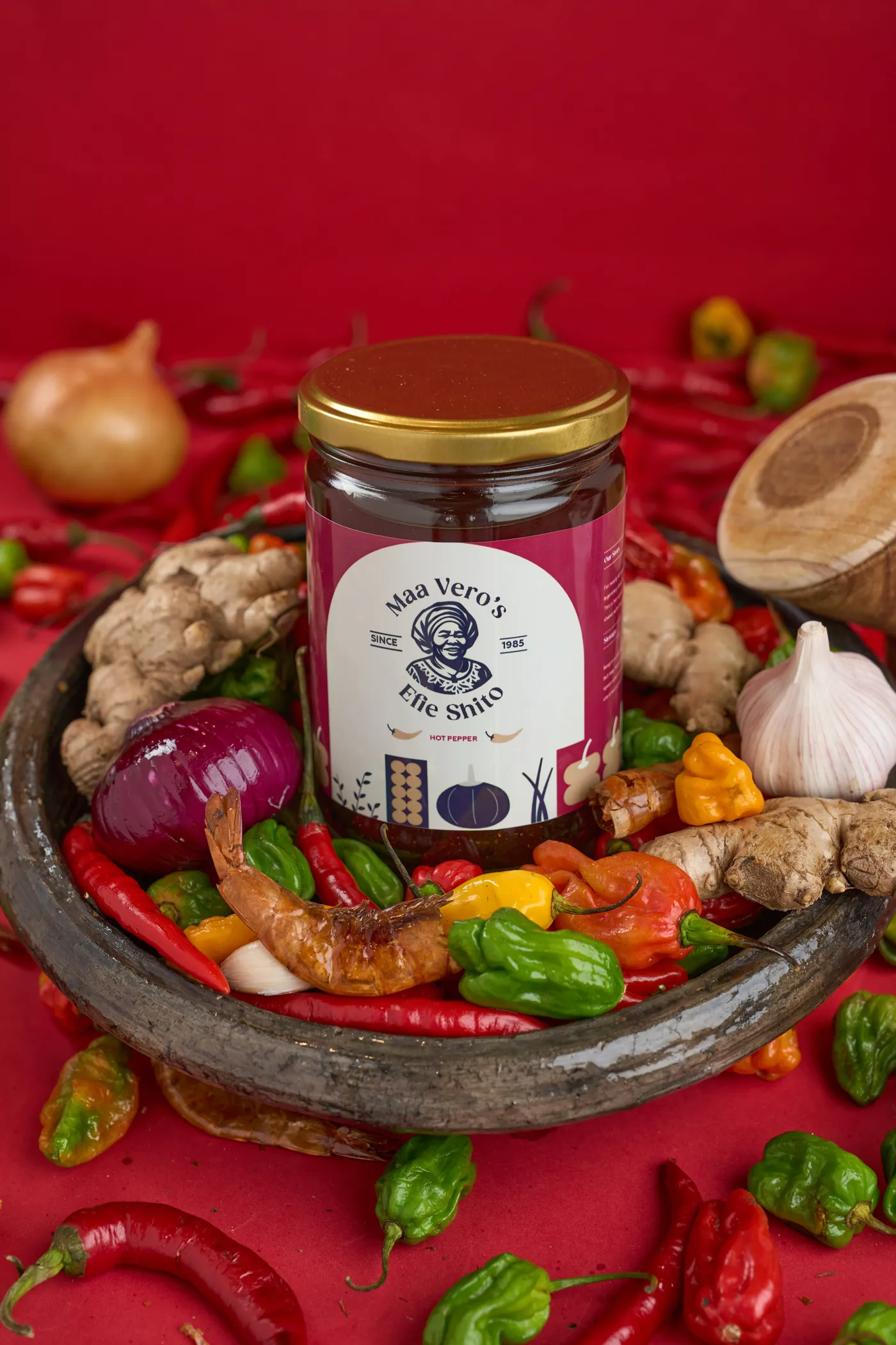 A jar of shito resting in a bowl of fresh peppers, onions and ginger