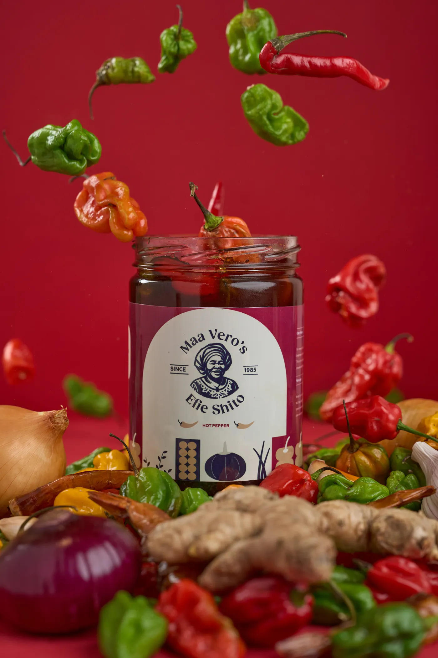 Fresh peppers bursting around a jar of Maa Vero's shito